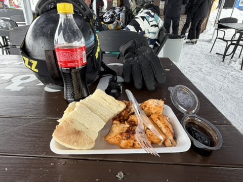 Gegrilltes Fleisch mit Brot und Cola auf dem Tisch neben Skihelm