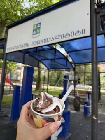 Soft-Serve-Eis in der Hand vor einem Schild der Gemeinde Lanchkhuti